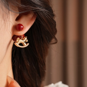 Close-up of gold-plated rocking horse earring with red stud and zircon detailing