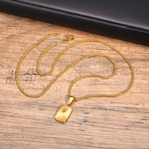 Detail of a square golden stainless steel pendant with radial texture on wood surface
