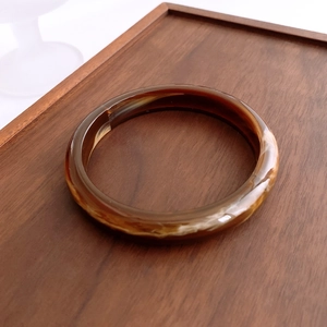 Detailed view of vintage amber acrylic bangle with tortoiseshell texture on wooden tray