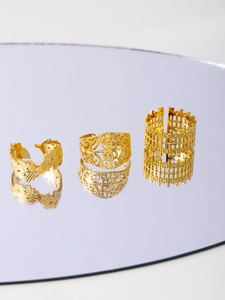 Detailed view of three gold mesh rings with feather, hollow, and crown motifs on a mirror
