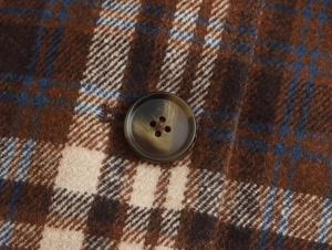 Detail of dark brown four-hole button on vintage plaid wool fabric coat surface
