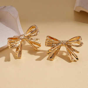 Golden bow stud earrings with pleated metallic texture on minimalist stone background