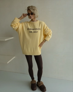 Detail of light yellow knit oversized sweater with ALSON CLUB text on textured fabric