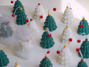 Detail of mini Christmas tree candles in green and white with red pom-poms in gift boxes
