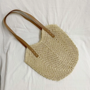 Detail of beige handwoven straw tote with brown leather straps and reinforced stitching