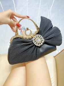 Close-up of black pleated bow evening bag with sparkling rhinestones and gold handle