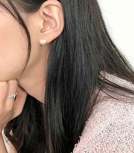 Close-up of heart-shaped pearl stud earrings and matching silver ring worn by a model