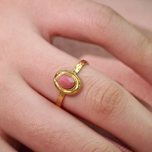 Close-up of a hammer-textured gold ring featuring an oval pink natural stone inlay