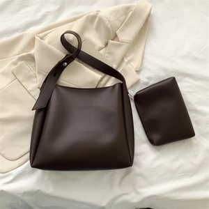 Detail view of large dark brown tote bag with matching pouch on beige suit