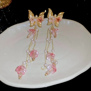 Détail de boucles d'oreilles à pompons avec papillons dorés et fleurs roses