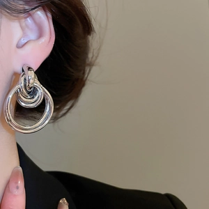 Close-up of polished silver layered intertwined hoop earrings worn by a model