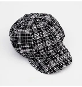 Close-up of black and white glen check newsboy cap with decorative button and woven texture