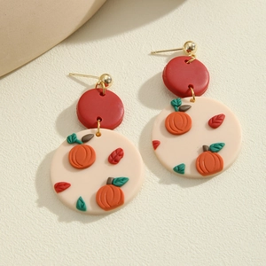 Detailed close-up of handmade clay pumpkin earrings with red top and autumn leaf accents
