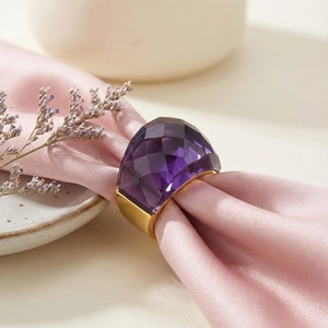 Detailed view of an 18k gold plated ring with a large purple faceted crystal on silk fabric