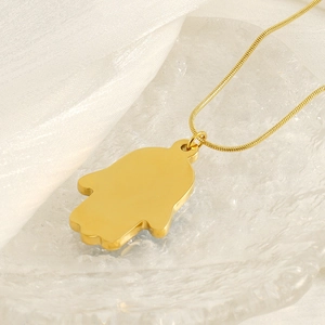Golden Hamsa Hand pendant on a snake chain over a glass plate and white silk fabric