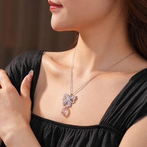 Detail of silver necklace with pink teardrop crystal and bow pendant on model's neck