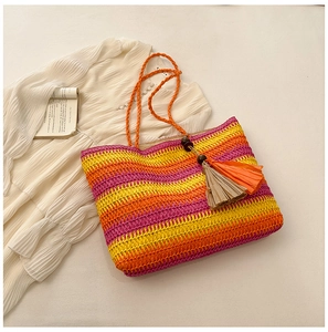 Detail of colorful striped straw tote bag with woven handles and tassels on a beige fabric