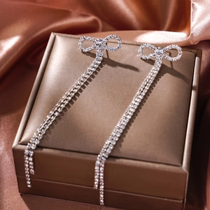 Macro shot of bow-shaped stud earrings with double rhinestone tassel fringe on silk