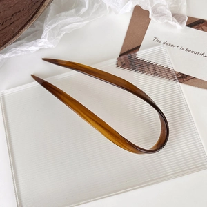 Detail showing amber tortoiseshell U-shaped hair pin on a textured glass block