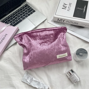 Flat lay of a plush purple velvet makeup bag with logo on a white fabric background
