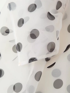Detailed view of white organza fabric with black polka dots and fine stitching textures