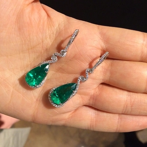 Dettaglio macro di orecchini a goccia con smeraldo e maglie in argento ondulate e zirconi