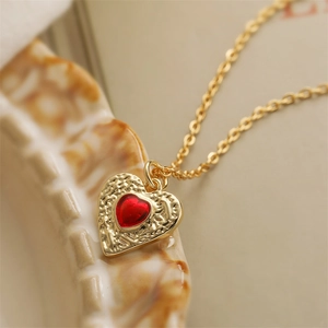 Vintage gold heart necklace with red enamel pendant on a patterned ceramic plate
