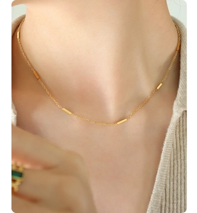 Detail of minimalist gold chain necklace with polished rectangular bar accents on model