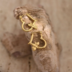 Macro shot of gold heart bee earrings on a natural stone background with high polish finish