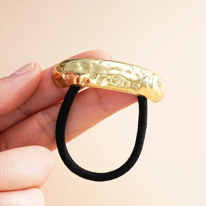Detailed close-up of a gold hammered metal bar on a black elastic hair tie for women