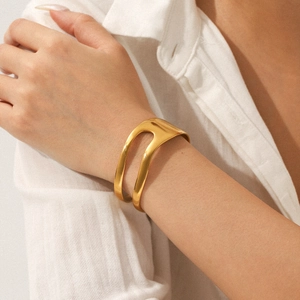 Detail of an asymmetric open gold bangle featuring a polished 18K plated stainless steel finish