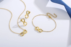 Detailed set of gold infinity symbol necklace, bracelet, and stud earrings on white background