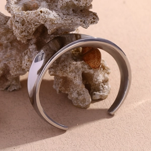Detailed close-up of polished silver geometric open bangle displayed on coral and shell