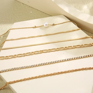 Detailed view of layered gold chain necklaces with pearls on a beige display tray
