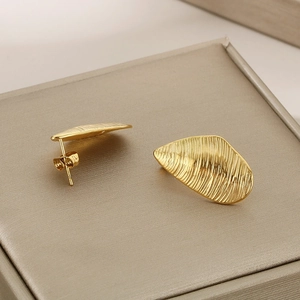 Detailed view of golden irregular teardrop stud earrings with textured vertical stripes