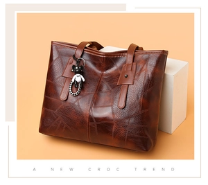 Detail view of brown croc-textured tote bag with cute animal charm on white cube