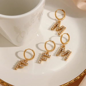 Detail of gold letter F and M earrings with cubic zirconia on a white plate