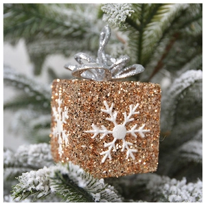 Detail of golden sequined Christmas gift box ornament with snowflake on a snowy tree