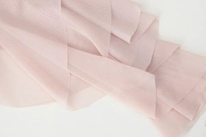 Detail shot of sheer pink mesh fabric featuring delicate pleats and soft layered textures