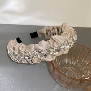 Detail of champagne satin pleated headband with sparkling rhinestones by a glass