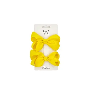 Pair of bright yellow grosgrain ribbon bow hair clips on a white fashion display card