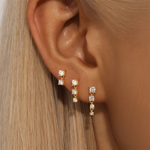 Close-up of three gold S925 silver stud earrings with round zircons worn on the ear