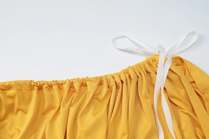 Detailed view of yellow dress waist featuring elastic smocking and white drawstring tie