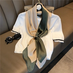 Detail of a beige and green striped silk scarf styled on a leather sofa with accessories