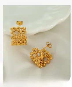 Close-up of 18K gold-plated C-shaped mesh bead stud earrings on a ceramic dish