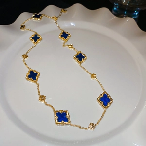 Detailed view of gold-plated necklace featuring blue quatrefoil clover charms on a tray