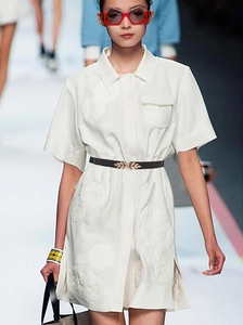 Detail of a thin black elastic waist belt with a golden leaf buckle on a white dress