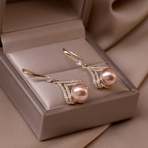Elegant champagne pearl earrings with gold V-shaped crystal accents on silk fabric