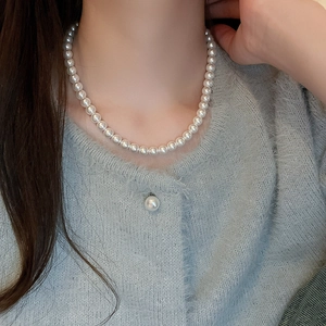 Close-up of elegant white round pearl necklace worn by a model in a grey cardigan