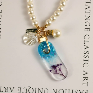 Macro detail of August tag and resin pendant with purple dried flowers on pearl necklace